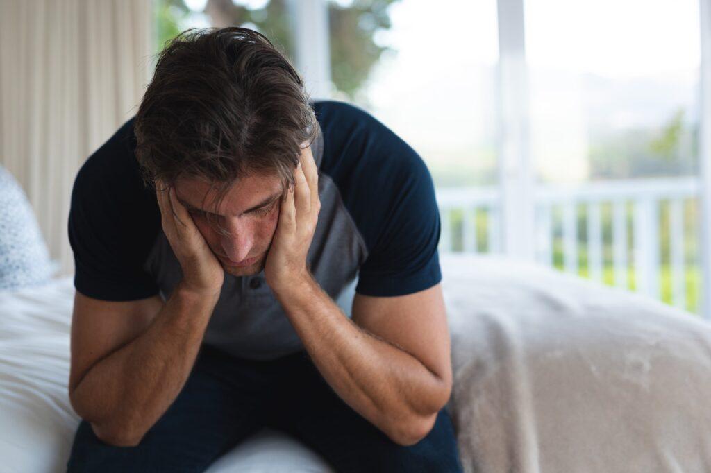 Worried man head in hands on the bed at home